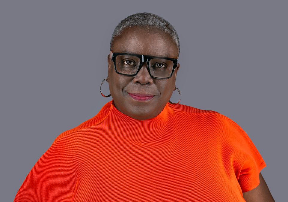 Head and shoulders of Cllr Williams wearing bright orange top and glasses smiling