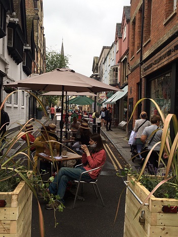 Several people dining outside on a high-street in Oxford under umbrellas