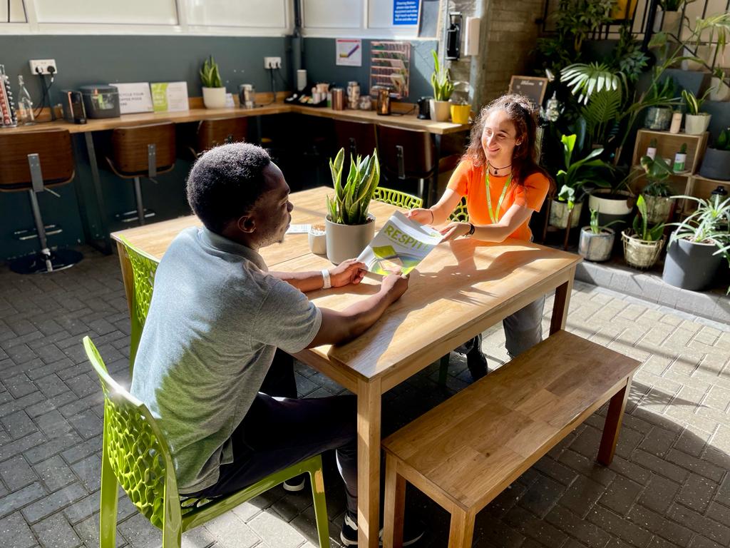Two people sitting at a table in Lancaster West Neighbourhood Team offices at Baseline Studios talking and sharing information