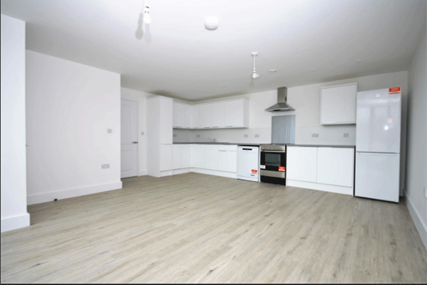 The inside of a new kitchen with white units and a wooden floor inside a new housing complex