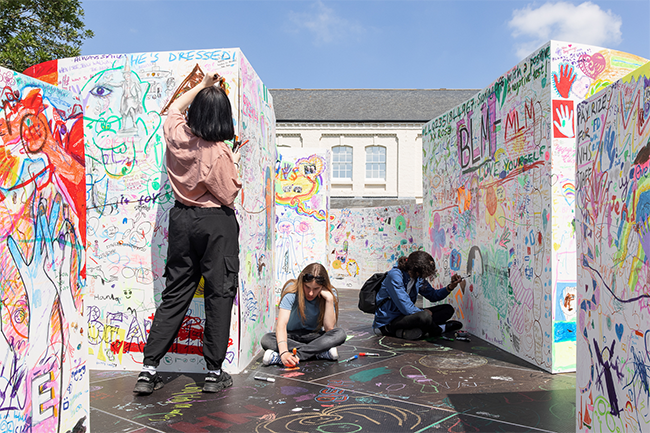 There are large white structures covered in drawing and writing. Three people are adding to the drawings.  