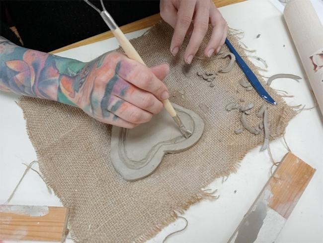 Woman's hands using clay tool to make a tile.    
