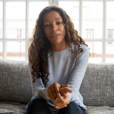 Young woman with long hair and grey jumper talking to camera