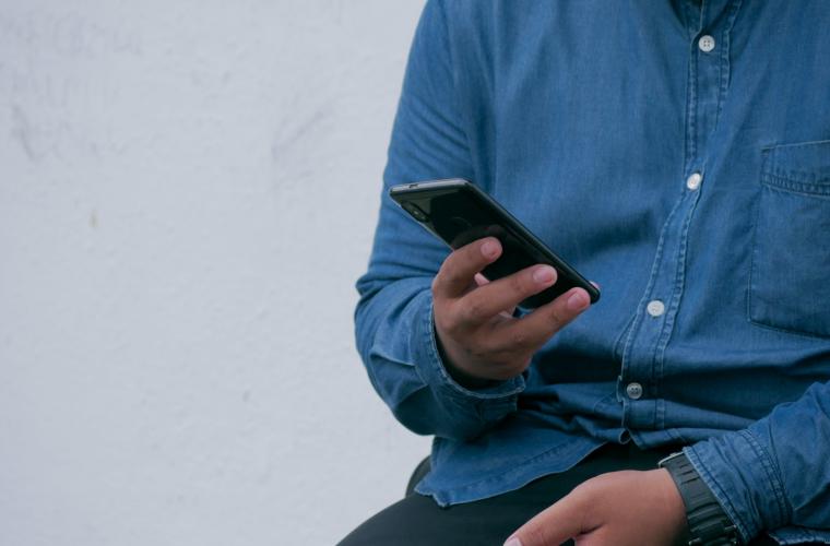 Person in a blue denim shirt holding a smart phone