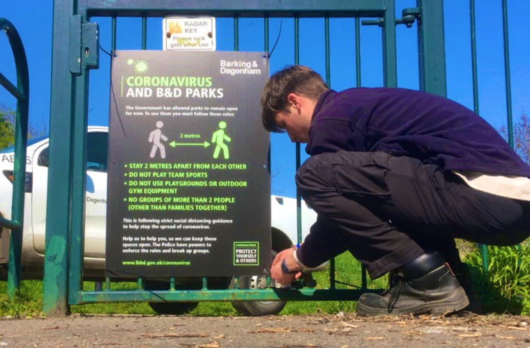 A man tying a COVID sign to a park fence