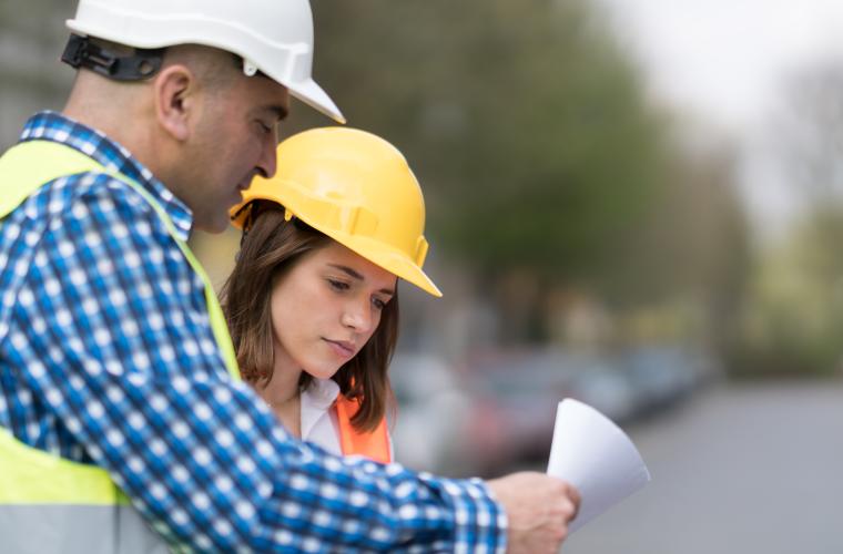 Young female engineering apprentice standing by a man looking at a document