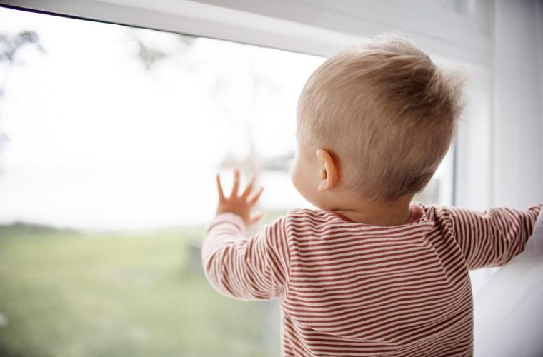 child in red striped shirt looking out the window