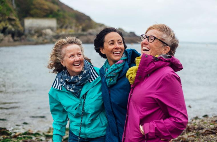 Three older women laughing on a walk on a cliff top by the sea