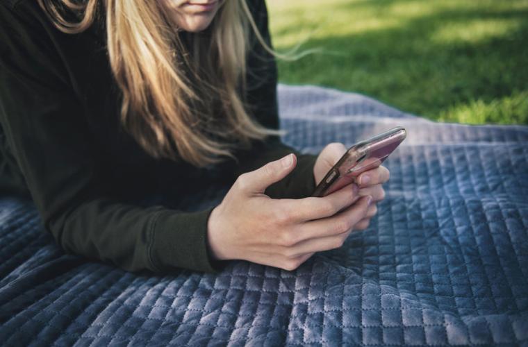 Woman lying on a blanket in a park holding a mobile phone