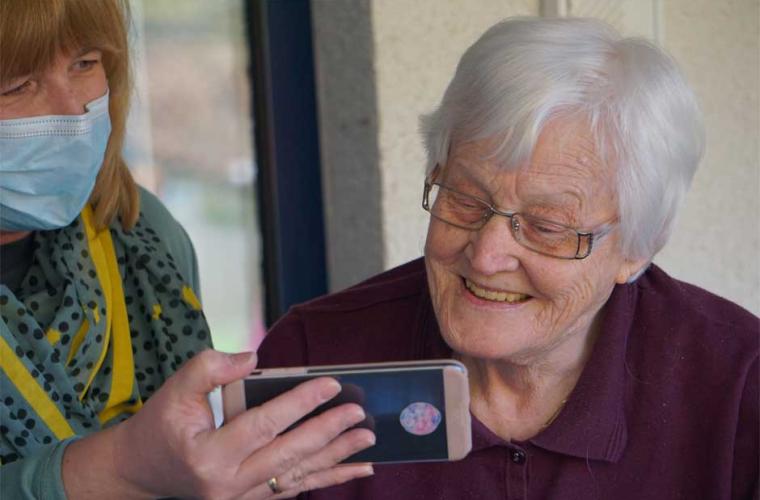 adult social care - woman in mask holding phone up to old lady