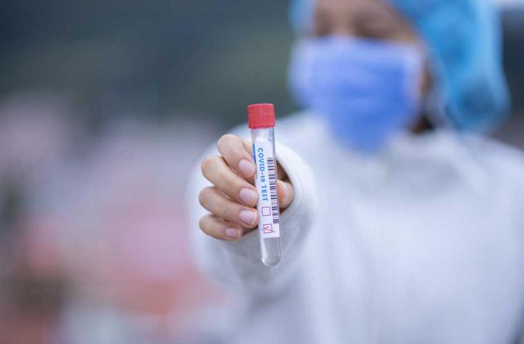 covid tester in a mask holding a vial 