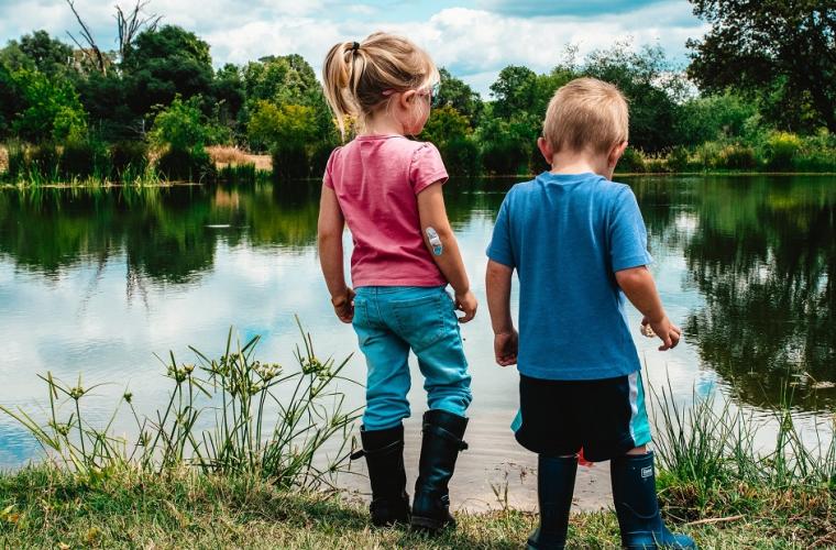 girl and boy standing on green grass near lake during daytime