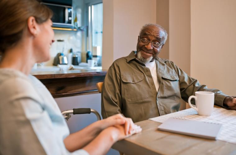 Person drawing on care sat at a table with a mug of tea and papers looking at smiling care worker