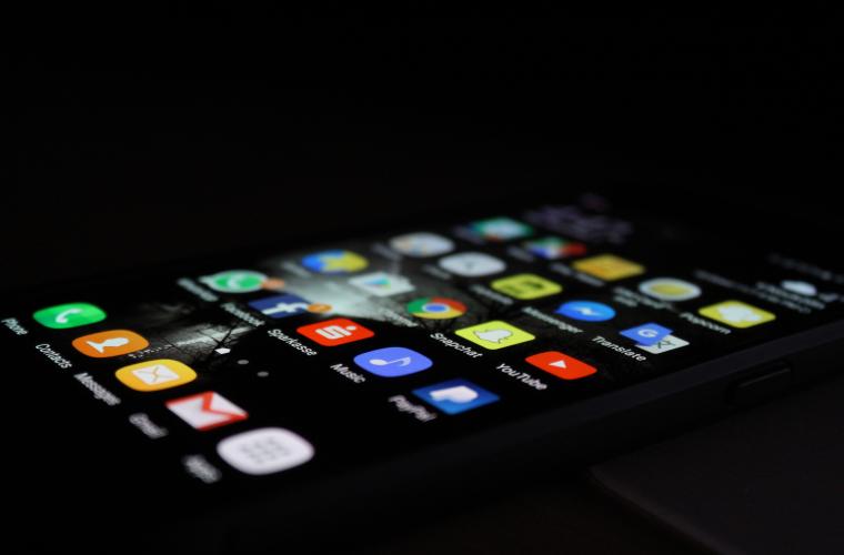 A dark background but the iPhone is lit up with the person's home screen and visible are all the different apps they have on their phone including YouTube, Snapchat, Facebook and Whatsapp