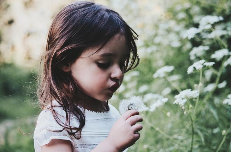 Little girl in white dress blowing a dandelion