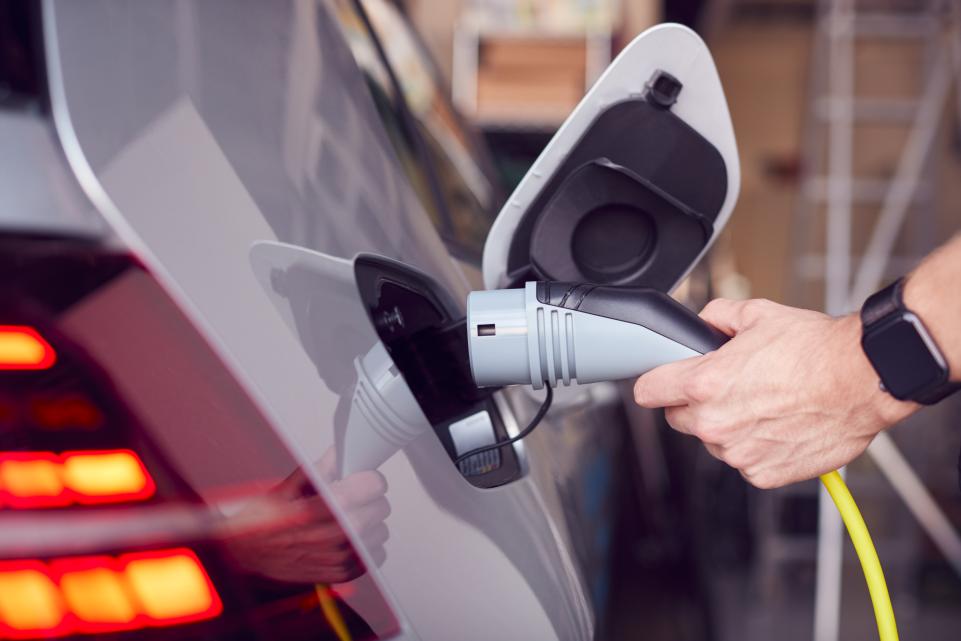 Hand holding electric vehicle recharger in car charging point