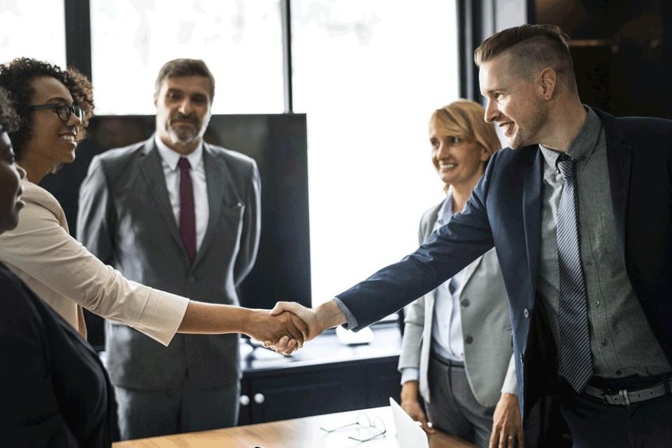 A group of people in an office in formal dress, with two shaking hands.