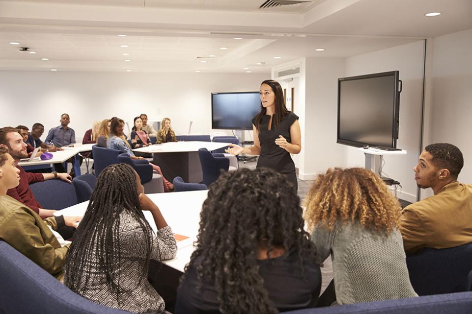 Woman standing and leading discussion surrounded by a group of people in a meeting room